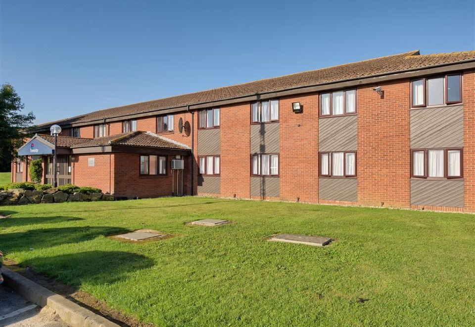 a red brick building with a grassy courtyard in front of it , under a clear blue sky at Travelodge Sleaford