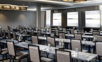 a conference room with rows of tables and chairs , a projector screen , and two large screens at Cambria Hotel West Orange