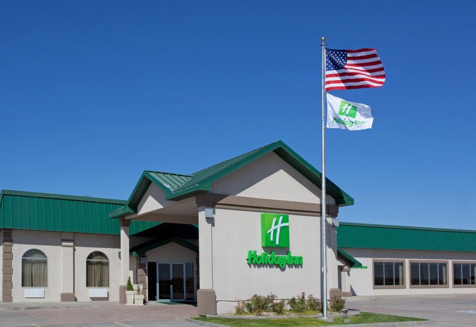a holiday inn hotel with a green roof and american flags flying in front of it at Country Inn & Suites by Radisson, Sidney, NE