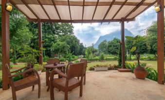 a patio with a wooden table and chairs , surrounded by trees and overlooking a mountainous landscape at Aurora Resort Chiangdao