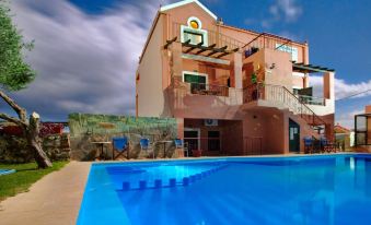 a large pink building with a blue swimming pool in front of it , surrounded by grass and trees at Olive Tree