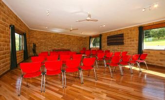 a conference room with red chairs arranged in rows and a television mounted on the wall at Alstonville Country Cottages