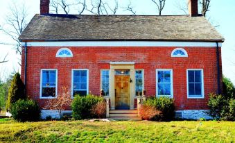 a red brick house with white trim , surrounded by green grass and trees , located in a rural area at Elmrock Inn