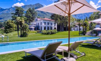 a large white house with a pool in the backyard , surrounded by lush green grass and trees at Villa Lario Resort Mandello