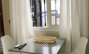 a small dining table with white chairs and a vase in front of a window at La Palmera Rooms
