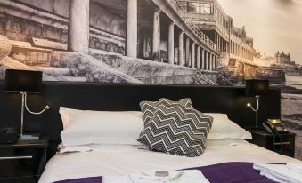 a black and white photo of a building is on the wall above a bed with a purple blanket at The Mayfield Seamer