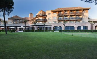 a large , two - story building with balconies and outdoor dining areas , surrounded by a lush green lawn and trees at DoubleTree by Hilton Islantilla Beach Golf Resort