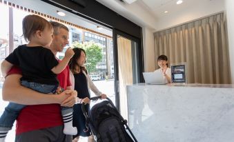 A group of individuals stands in front of the counter, observing a person who is seated, while holding their luggage at Sakura Cross Hotel Akihabara