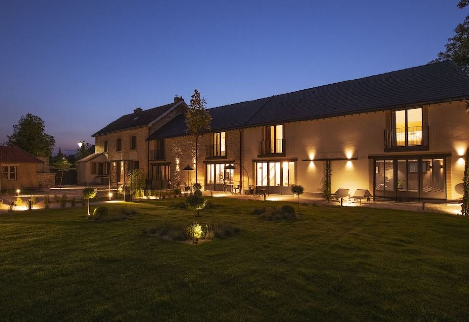 a large house with a well - maintained lawn and well - maintained trees , lit up at night at Au Clos du Lac