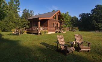 a wooden cabin surrounded by a lush green lawn , with two chairs placed on the grassy area in front of it at Opossum Creek Retreat