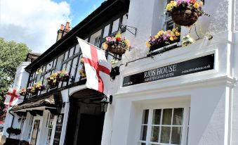 "the exterior of a white building with balconies , flowers , and a flag , as well as a sign for the "" riording" at Rioshouse George-Inn