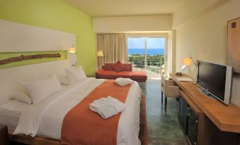 a hotel room with a large bed , orange and white bedding , and a view of the ocean at E-Hotel Larnaca Resort & Spa