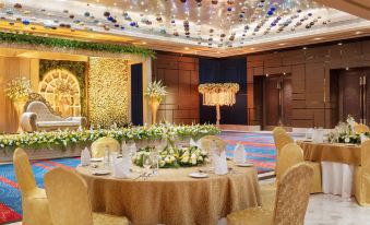 a well - decorated banquet hall with multiple dining tables set up for a formal event , including round tables , gold chairs , and flower arrangements at Sheraton Grand Bengaluru Whitefield Hotel & Convention Center