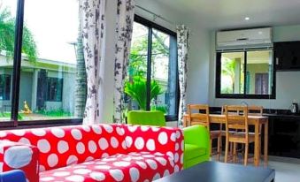 a brightly lit living room with a red and white polka dot couch , a dining table , chairs , and a television at Aroonsawad Riverview Resort