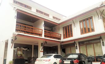 a large two - story house with a balcony on the second floor , surrounded by cars parked in front of it at The Indigo House Phrae