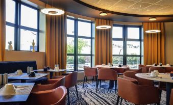 a modern dining room with multiple tables and chairs , creating a warm and inviting atmosphere at Novotel Paris 14 Porte d'Orleans