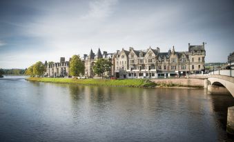 a row of houses along the edge of a body of water , with a boat visible in the distance at Columba Hotel Inverness by Compass Hospitality