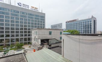 a modern building with a glass facade and a logo on the roof , surrounded by other buildings and cars at Airport Hotel