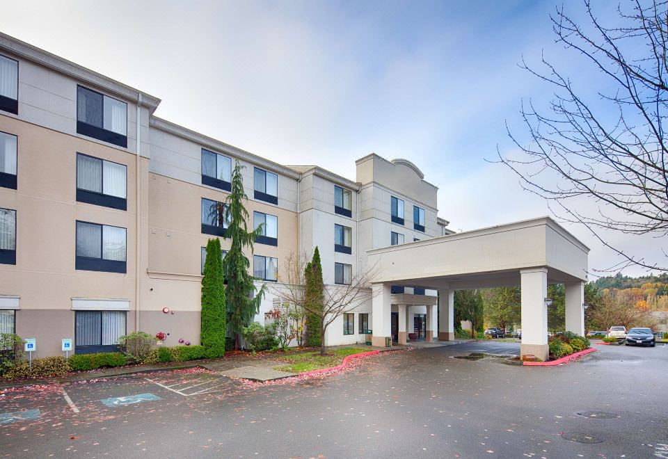 a large building with a covered entrance and parking lot in front of it , under a cloudy sky at Holiday Inn & Suites Bothell