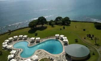 a large , oval - shaped pool is surrounded by lounge chairs and umbrellas in a resort setting at Pestana Bahia Praia Nature & Beach Resort