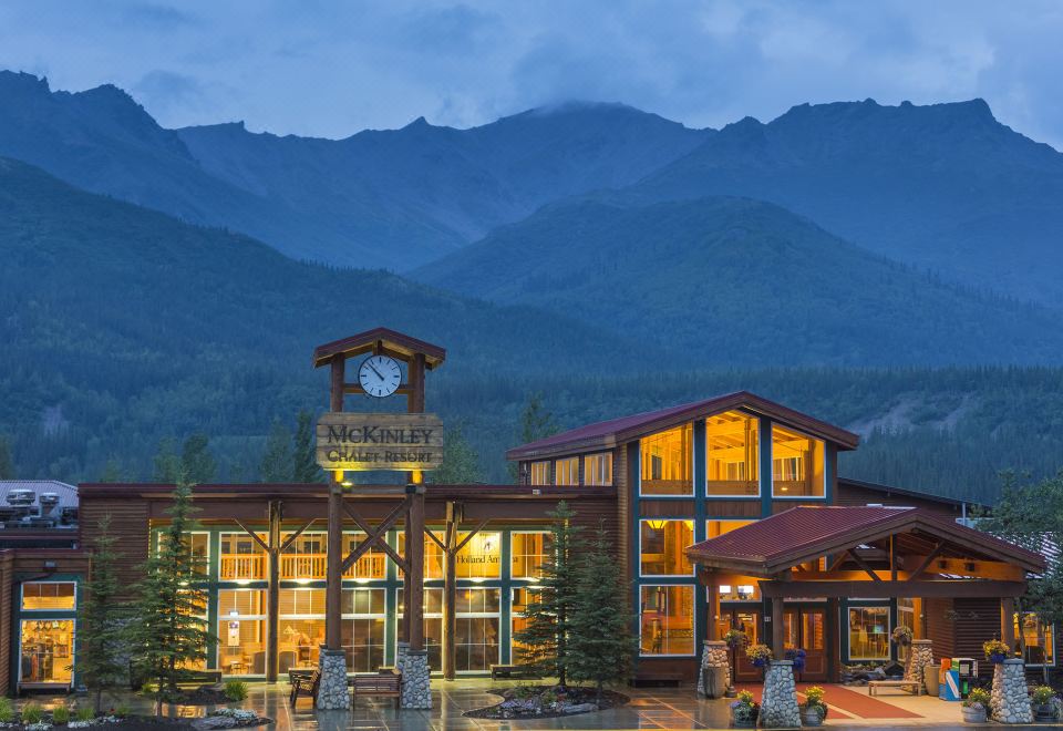 a large building with a clock on the front is surrounded by trees and mountains at McKinley Chalet Resort