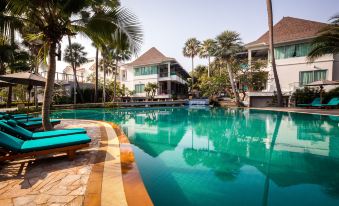 a large swimming pool surrounded by palm trees , with several lounge chairs placed around the pool for relaxation at Bann Pantai Resort