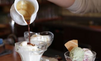 a person is pouring a drink from a pitcher onto a table with three bowls containing ice cream at Santa San