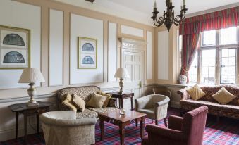 a living room with a chandelier , couches , and chairs arranged in a square formation around a central table at The Billesley Manor Hotel