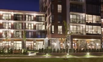 a modern apartment building with multiple balconies and windows , surrounded by trees and lit up at night at Oswego Hotel
