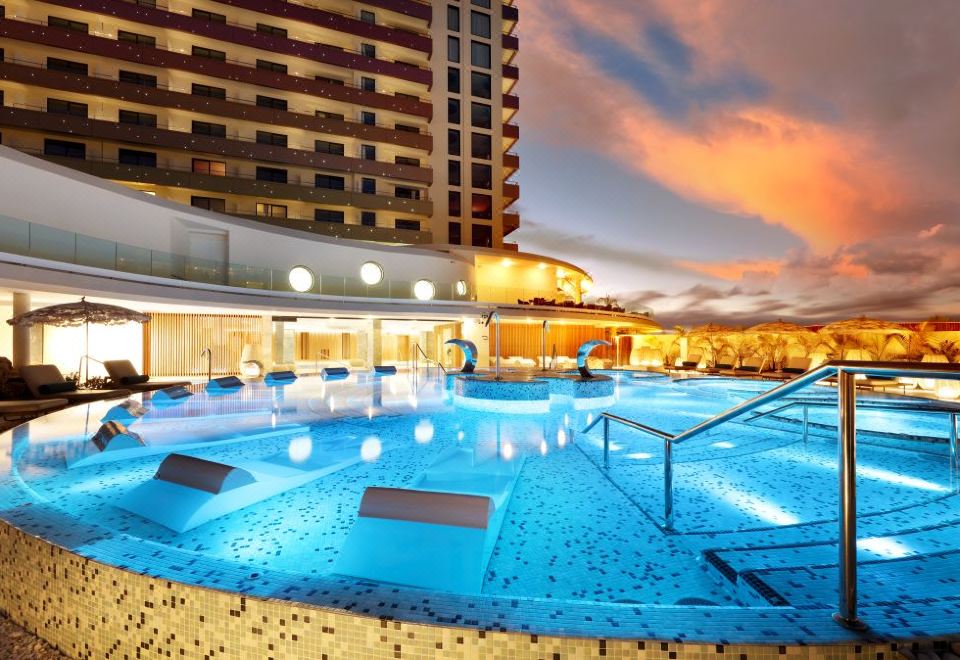 a large swimming pool with blue water and lights , situated in front of a tall building at sunset at Hard Rock Hotel Tenerife