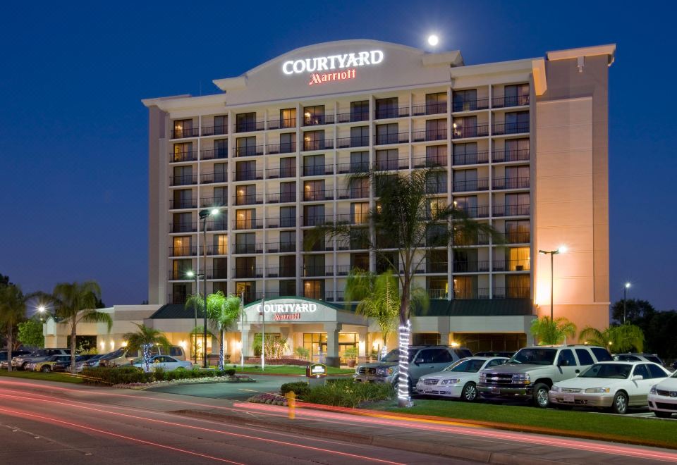 a nighttime view of a courtyard by marriott hotel , with its lights reflecting on the glass windows and palm trees in the foreground at Courtyard by Marriott Los Angeles Pasadena/Monrovia