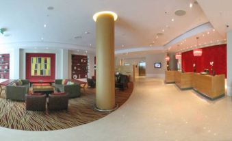 a modern hotel lobby with a large round pillar in the center , surrounded by various seating options at London Twickenham Stadium Hotel, a Member of Radisson Individuals