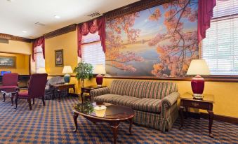 a cozy living room with a large painting of flowers on the wall , a couch , and two lamps at Clarion Inn Falls Church- Arlington