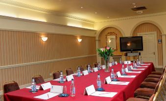 a long table with red tablecloth , water bottles , and name tags is set up in a room with yellow walls at Best Western Lamphey Court Hotel