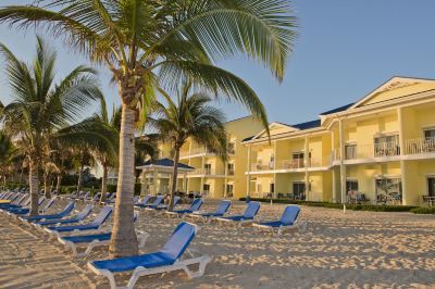 a beach scene with a row of blue lounge chairs and a palm tree in the background at Wyndham Reef Resort Grand Cayman