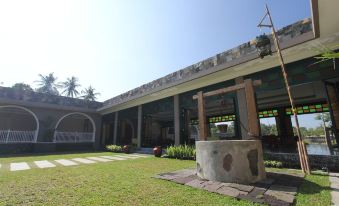 a large building with a stone wall and grass in front of it , surrounded by palm trees at The Westlake Hotel & Resort Yogyakarta