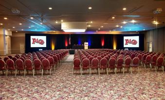 a large conference room with rows of red chairs arranged in a semicircle , and two large screens on either side of the stage at Plaza Hotel & Casino