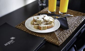 a plate of bread with whipped cream on a table , accompanied by two glasses of orange juice at AquaHotel