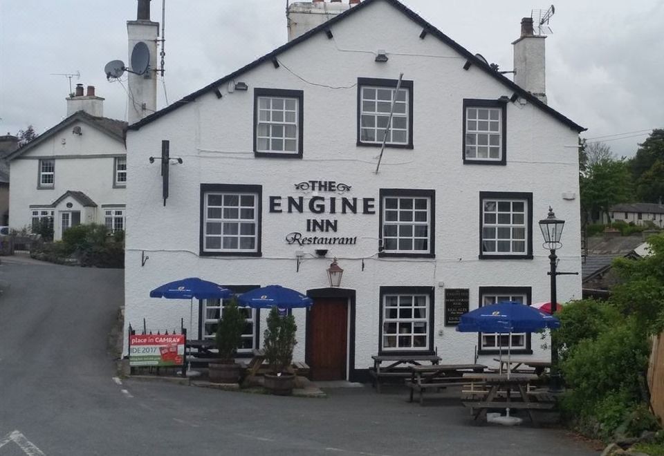 "a white building with a black sign that says "" the engine inn "" and blue umbrellas on the porch" at The Engine Inn