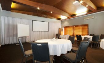 a conference room with a large white table surrounded by chairs and a projector screen at Dog Rock Motel