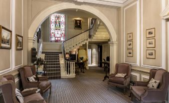 a large , ornate room with a staircase leading to the second floor and several chairs arranged in front of it at Eshott Hall