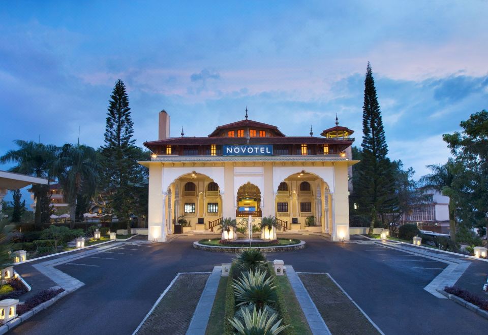 a large white building with a red roof , surrounded by trees and lit up at night at Novotel Bukittinggi