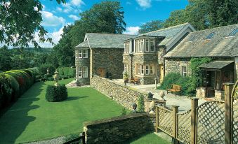 The front yard of a large stone house is surrounded by an old fence, and the lawn is covered in green grass at Sharrow Bay Country House Hotel