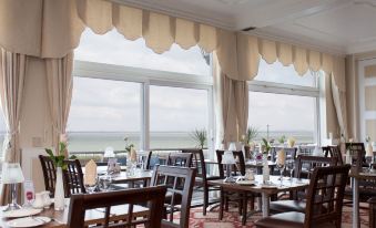 a dining room with wooden tables and chairs , along with a view of the ocean at Best Western New Holmwood Hotel