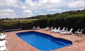 a large , rectangular swimming pool surrounded by chairs and umbrellas , with a clear blue sky overhead at Prom Coast Holiday Lodge