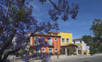 a colorful building with a yellow and orange exterior is surrounded by purple flowers , set against a clear blue sky at Marin Hotel