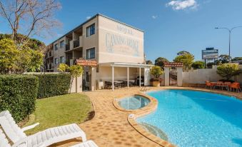 "a large swimming pool is surrounded by lounge chairs and a building with a sign that says "" canoga ""." at Canning Bridge Auto Lodge