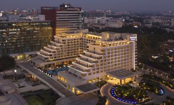 a large , modern hotel building with multiple stories and balconies , surrounded by trees and other buildings at Sheraton Grand Bengaluru Whitefield Hotel & Convention Center