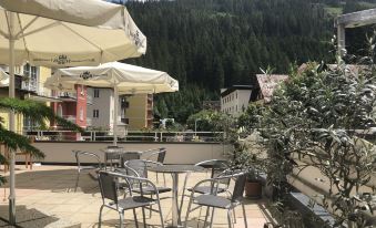 an outdoor dining area with umbrellas , tables , and chairs on a rooftop , surrounded by mountains in the background at Hotel Lindenhof
