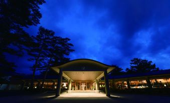 a modern , well - lit building with an open - air structure and trees in the background at night at Karuizawa Prince Hotel East